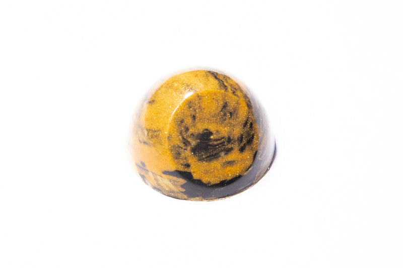 Praline in de vorm van een halve cirkel met afgeplatte kant, in donkerbruin en geel met glitters